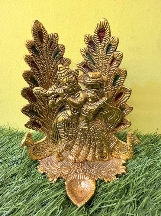 Peacock Design Radha Krishna Idol Showpiece with Diya. Ideal for Puja & Home Decor. Crafted in Metal with a Gold Finish. Size: 8x6 inches.