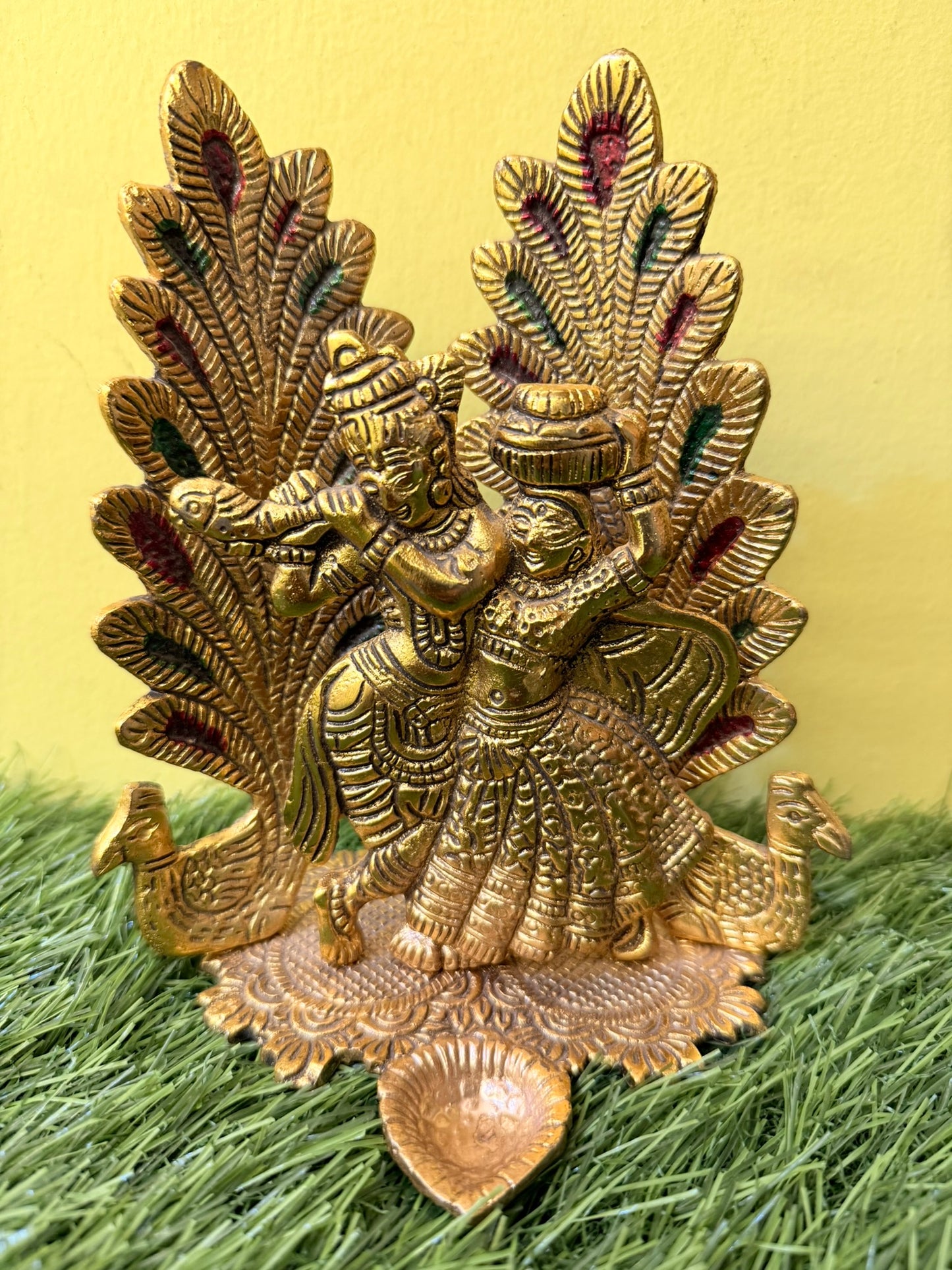 Peacock Design Radha Krishna Idol Showpiece with Diya. Ideal for Puja & Home Decor. Crafted in Metal with a Gold Finish. Size: 8x6 inches.